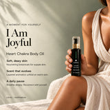 Woman in a linen dress holding I Am Joyful Heart Chakra Ritual Body Oil in black glass with a gold collar