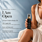 Woman in a linen dress holding I Am Open Throat Chakra Ritual Body Oil in black glass with a gold collar